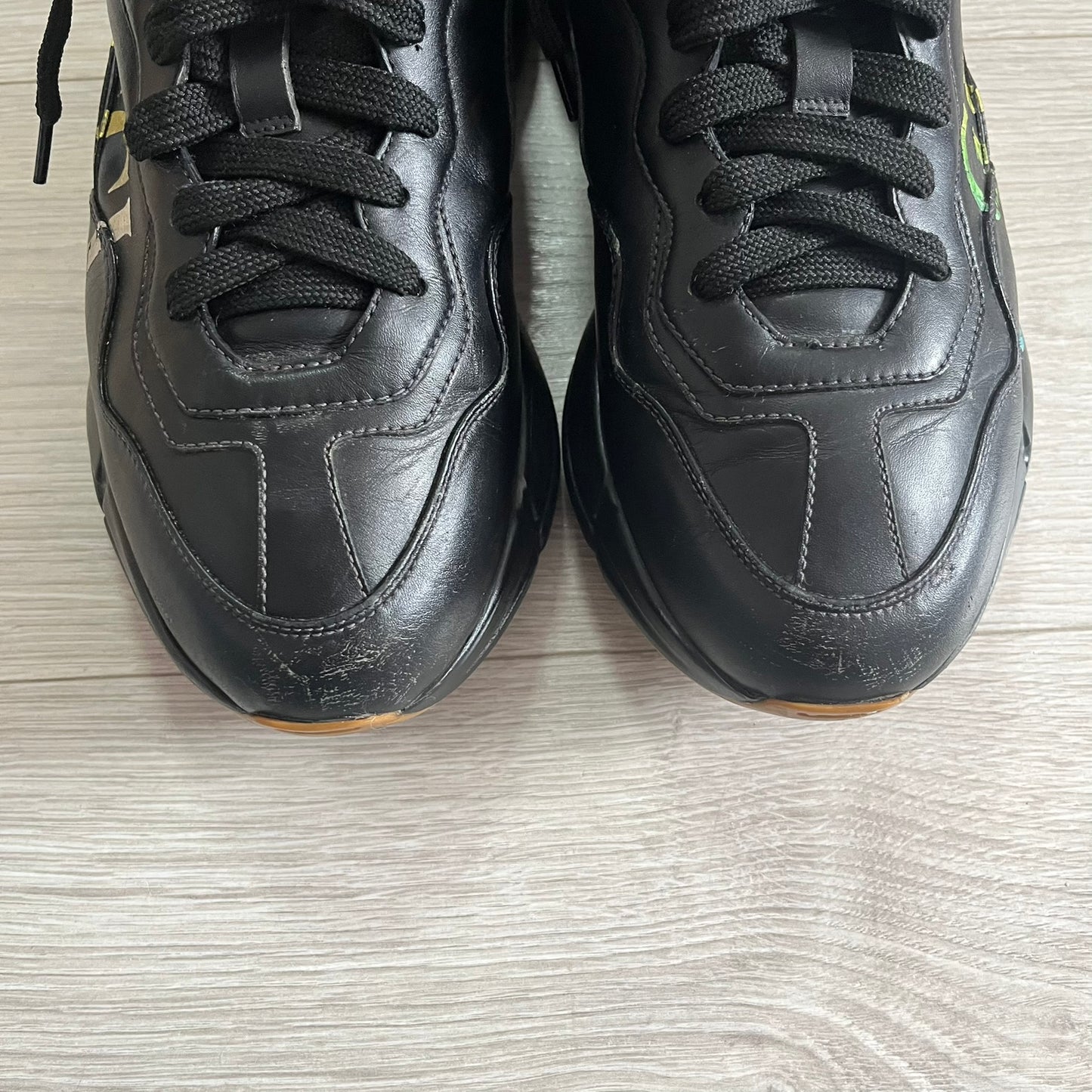 Pair of black sneakers on a light wooden floor.
