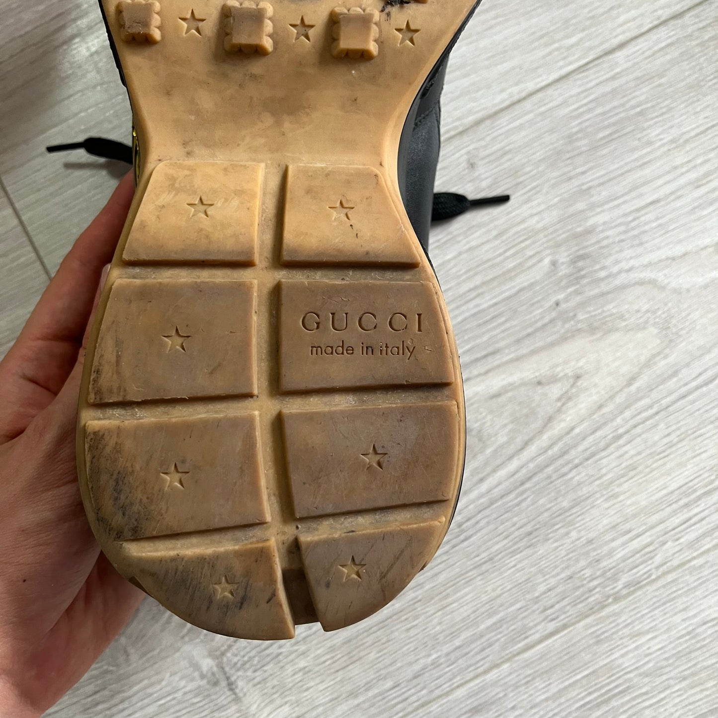 Close-up of a Gucci shoe sole with 'made in Italy' text on a light wooden floor.