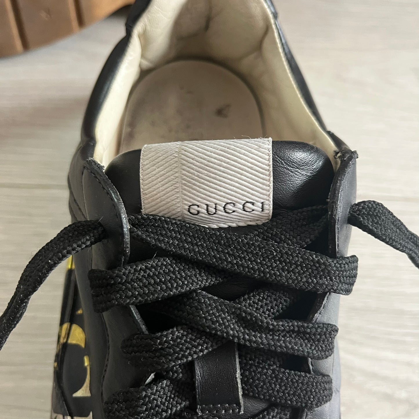 Black Gucci sneaker with laces tied, showing the brand logo on the tongue.