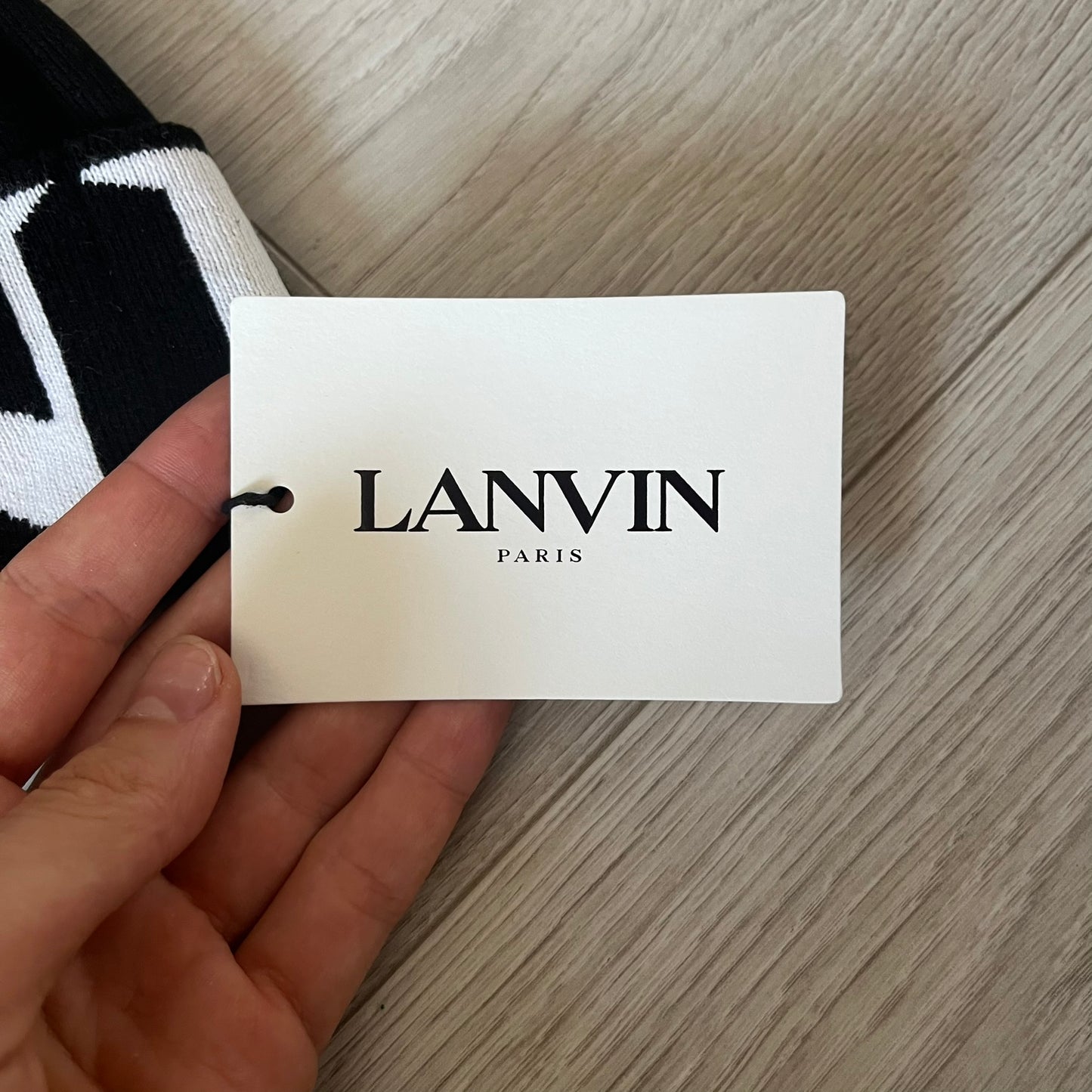 Hand holding a Lanvin tag on a wooden surface