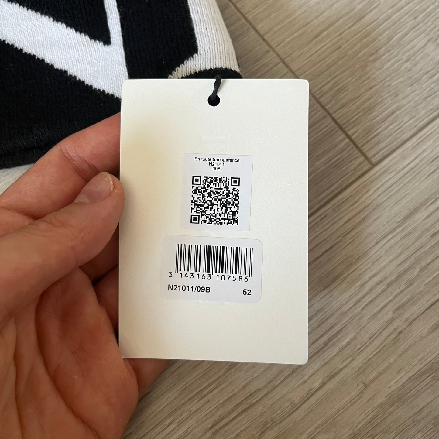 Hand holding a product tag with QR code and barcode on a wooden surface