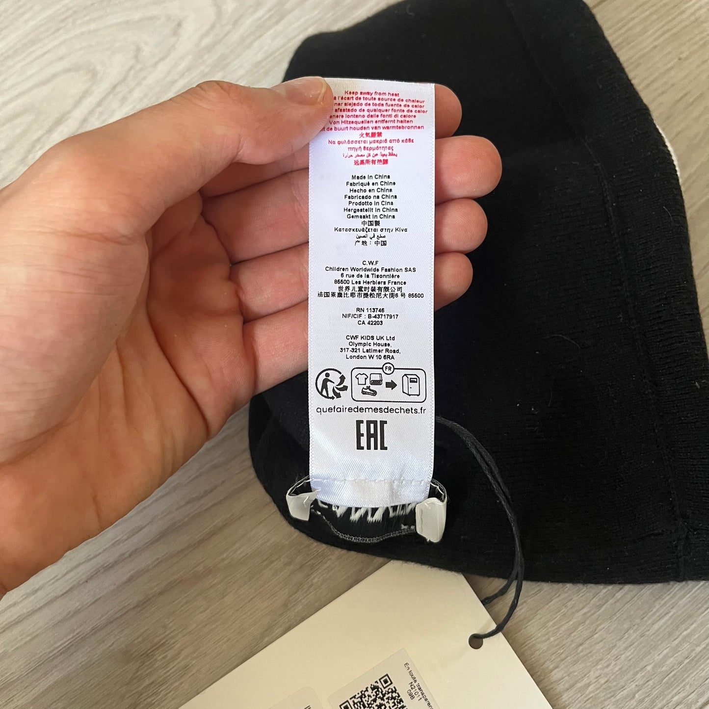 Hand holding a black sock with a visible label on a light wooden surface