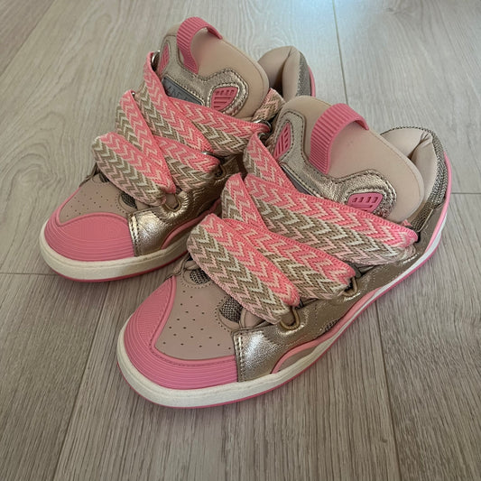 Pair of pink and gold children's sandals on a wooden floor