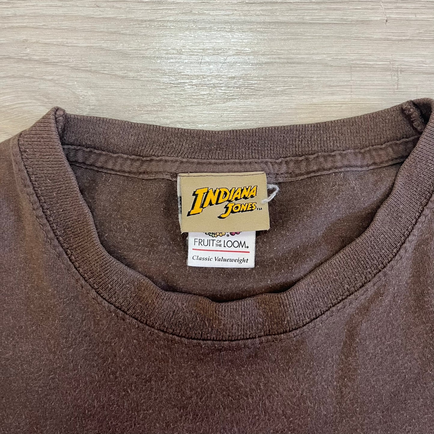 Brown shirt with 'Indiana Jones' tag on a wooden surface