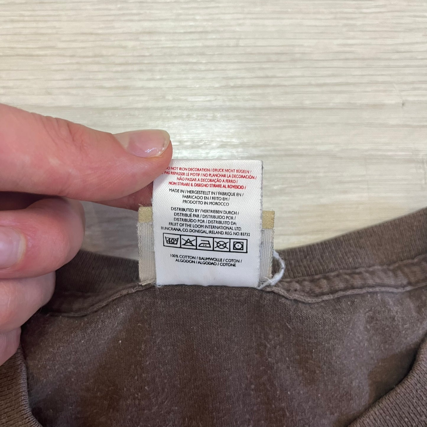 Close-up of a clothing label on brown fabric with a hand holding it.