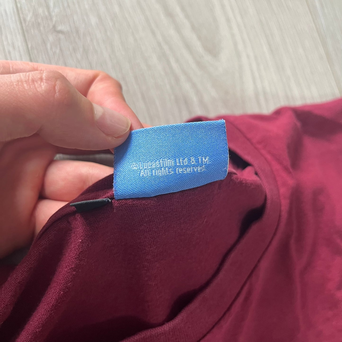 Hand holding a blue label on a maroon garment with a light wooden surface in the background