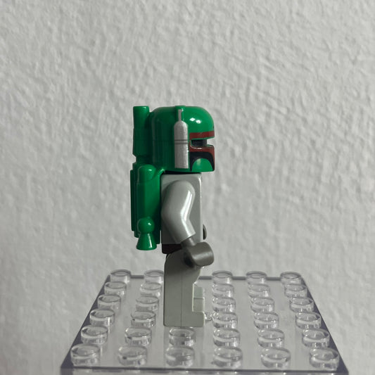 Green and gray Lego figure on a clear baseplate against a white wall