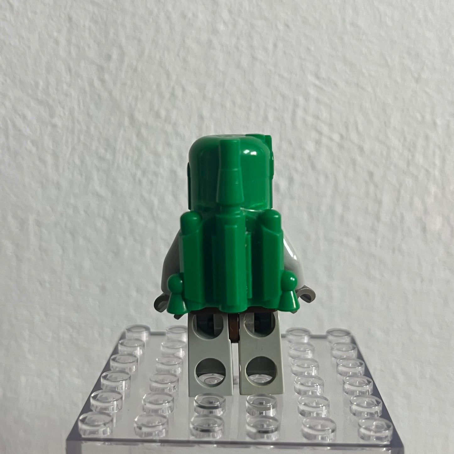 Green toy figure on a clear baseplate against a white background
