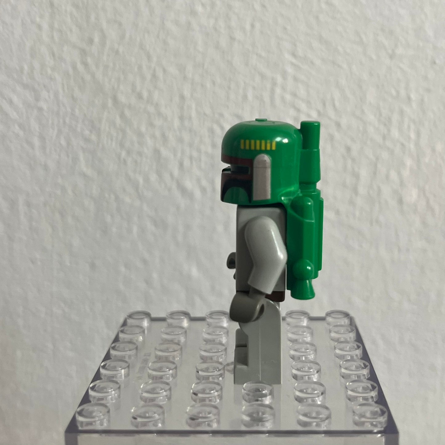 Green and gray robot figure on a clear base against a white wall