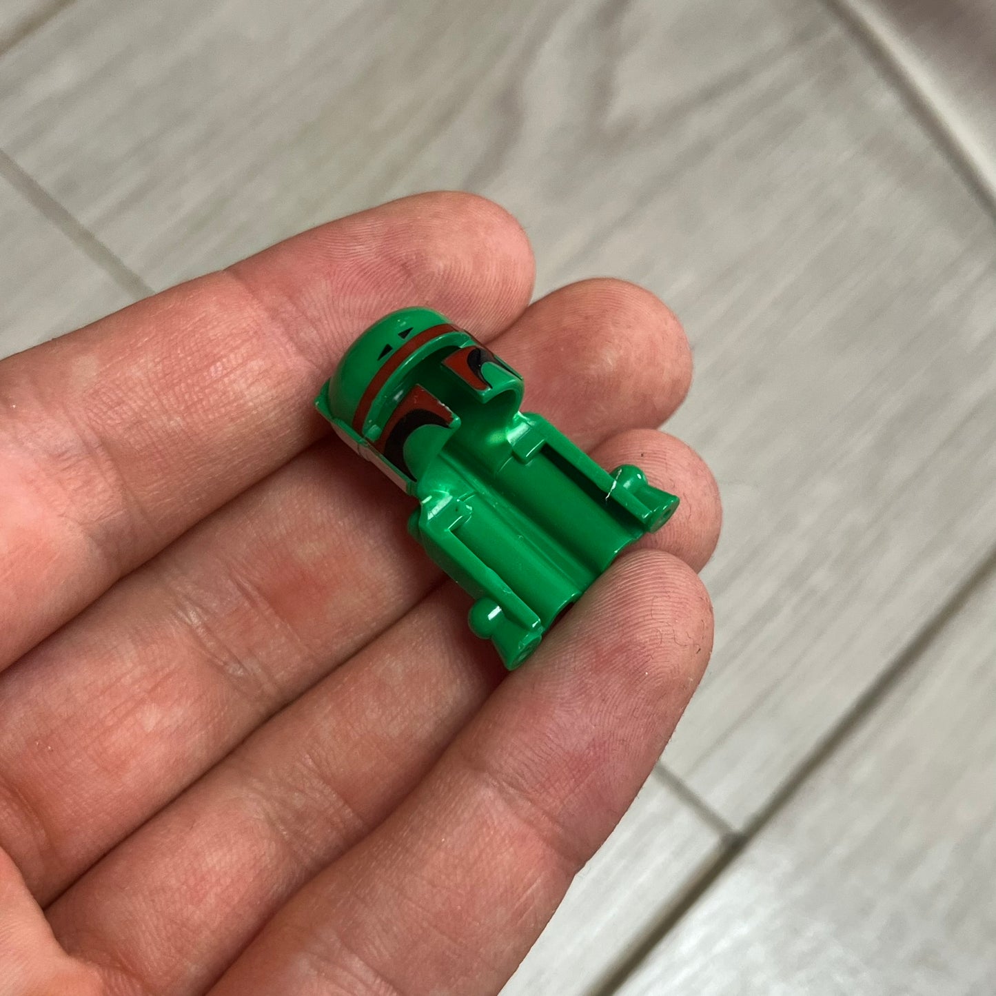 Small green plastic object held in a hand on a light wooden surface