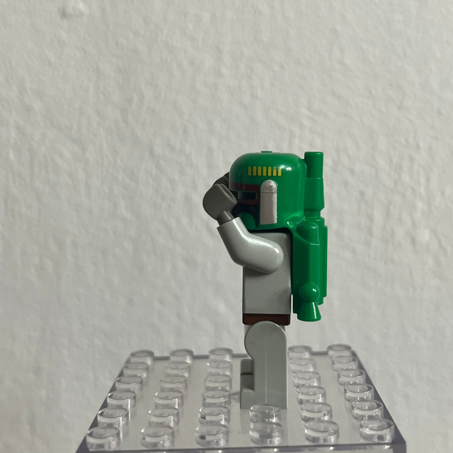 Green and gray Lego figure on a clear baseplate against a white background