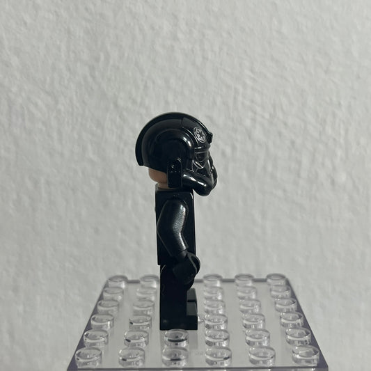 Black LEGO figure on a clear baseplate against a white wall