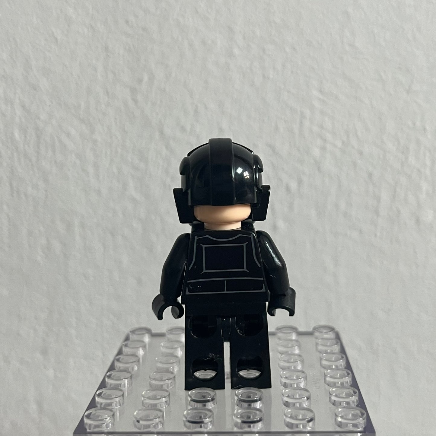 Black LEGO minifigure with helmet on a clear baseplate against a gray background