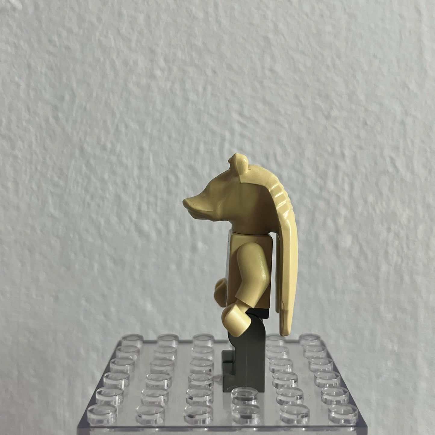 Gold-colored figure on a clear baseplate against a white wall
