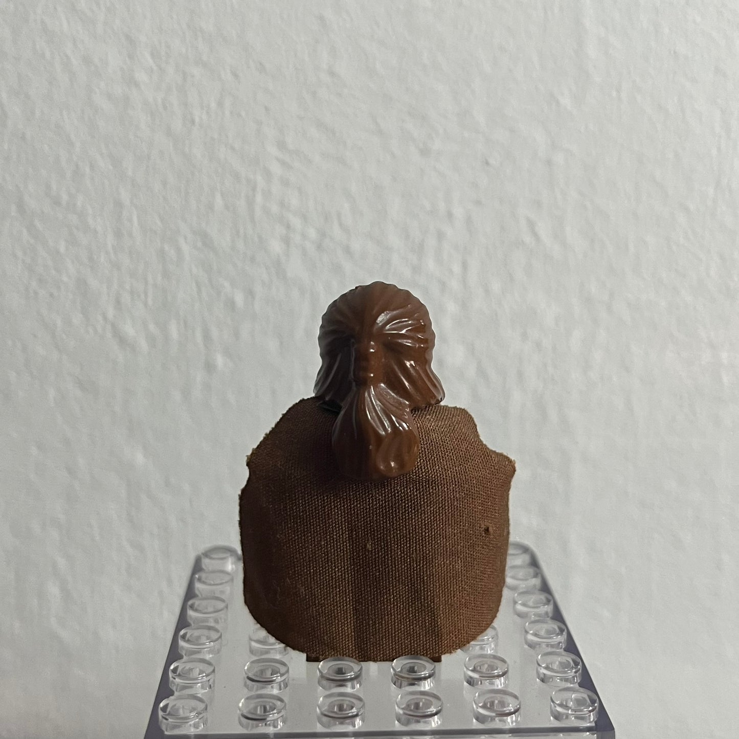 Small brown figure on a clear plastic base against a white wall