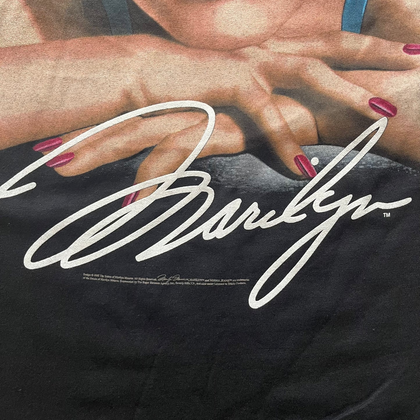 Close-up of a black shirt with a signature and hands wearing red nail polish.
