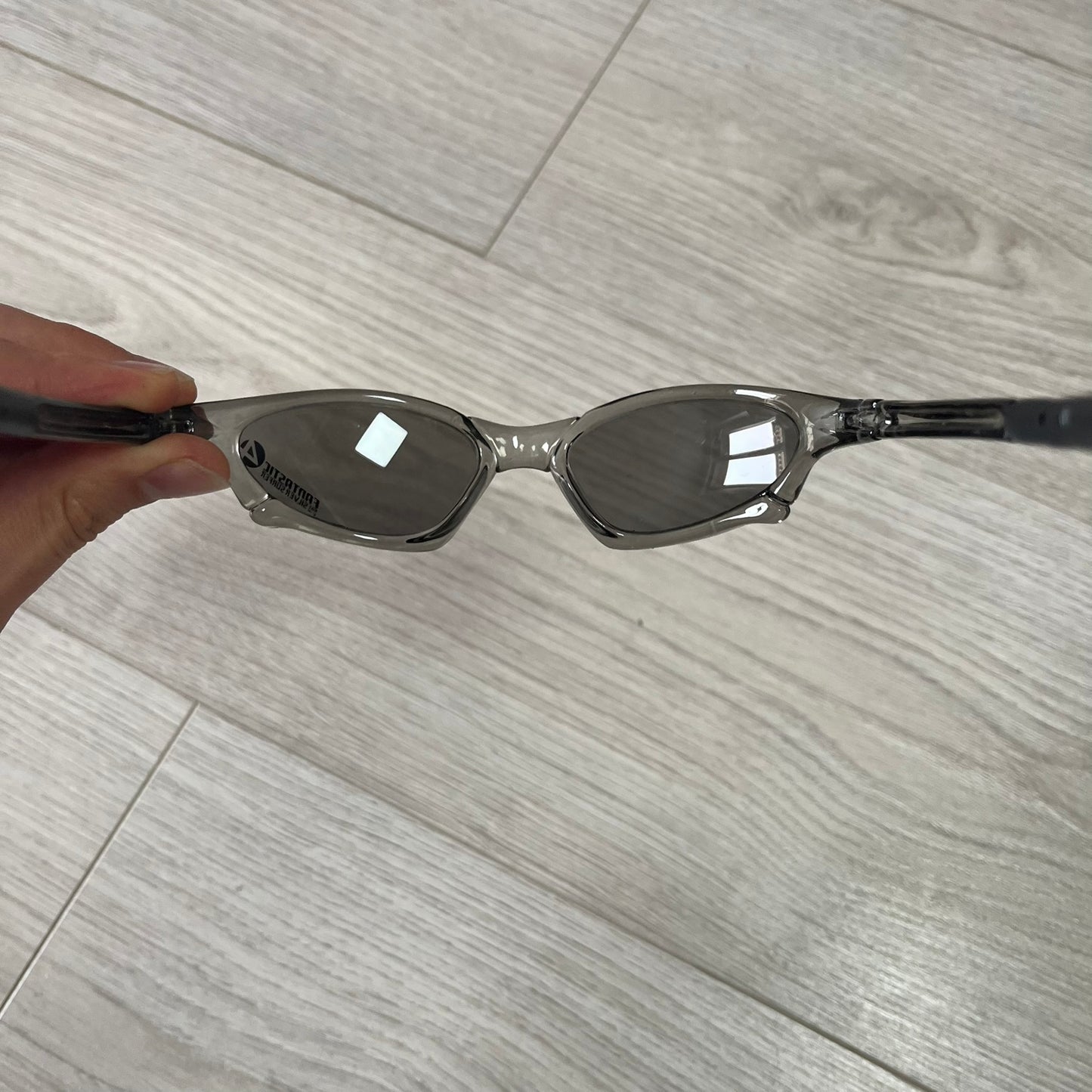 Sunglasses held by a hand on a wooden floor