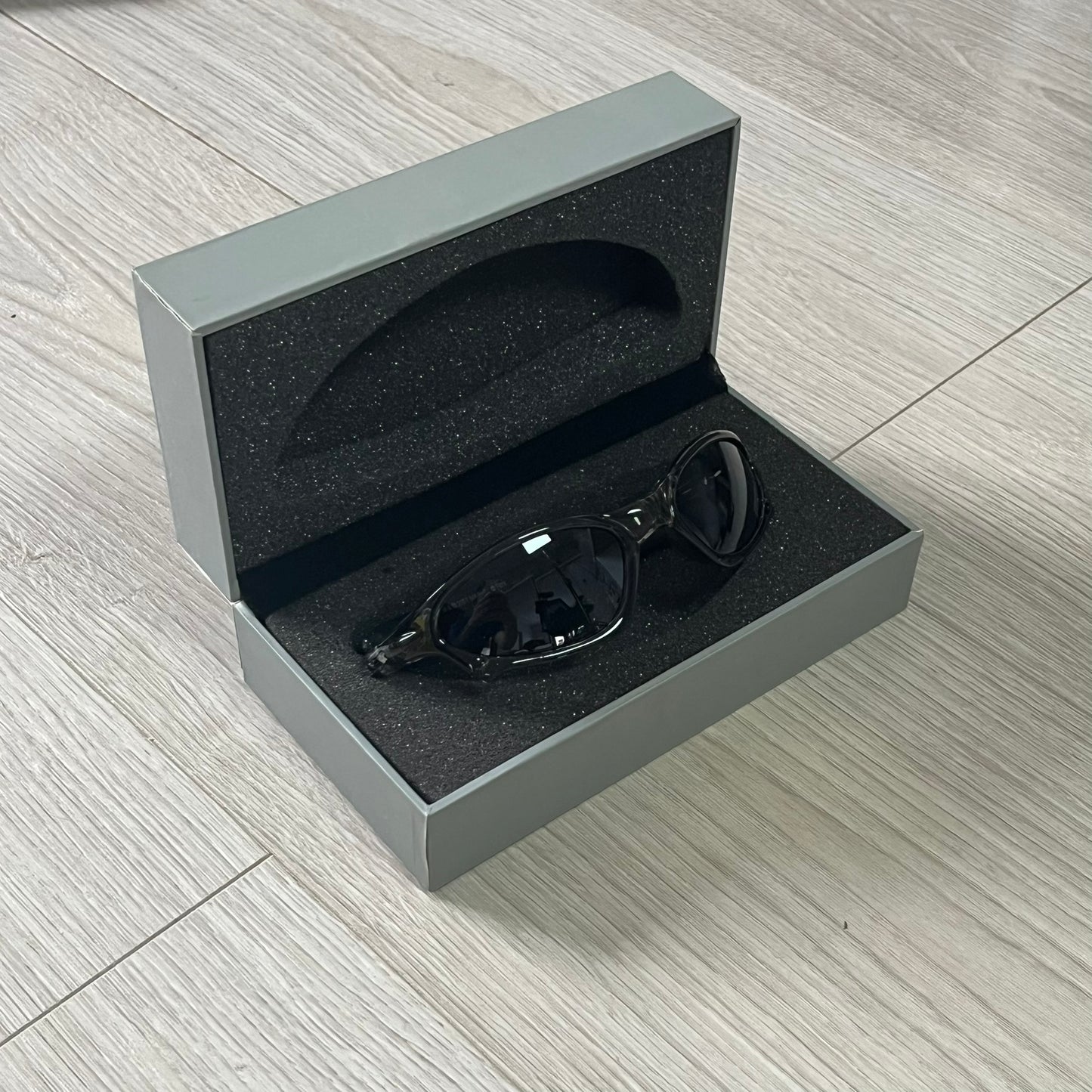 Black sunglasses in a gray open box on a wooden floor