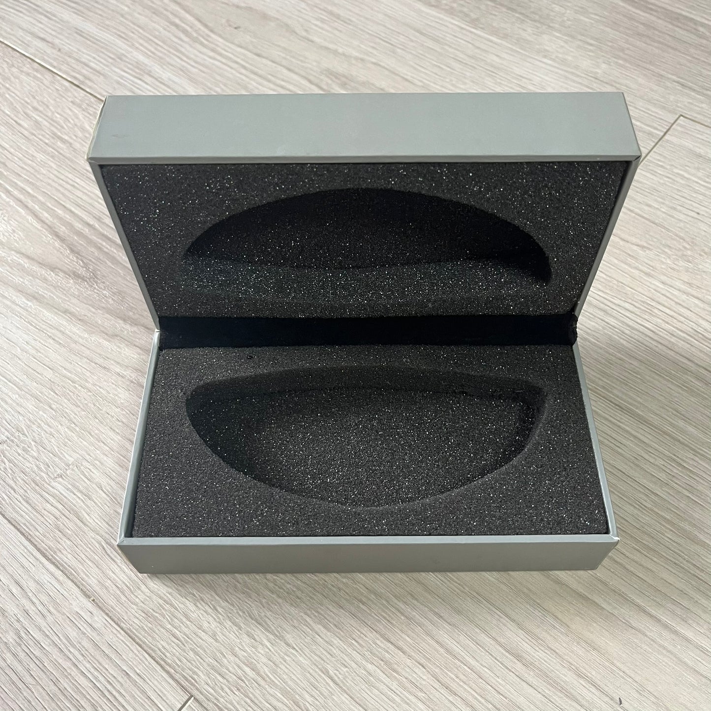 Open gray box with black interior foam on a light wooden surface