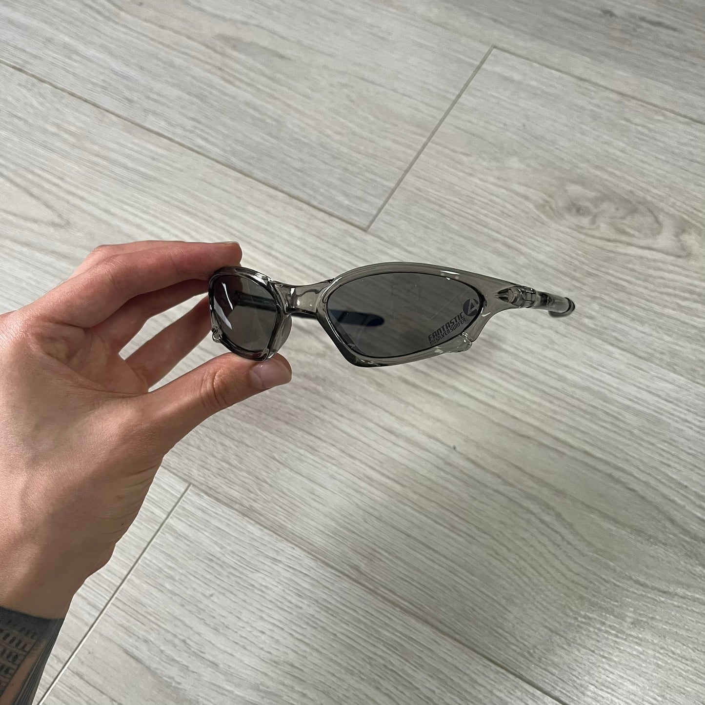 Sunglasses held by a hand on a wooden floor