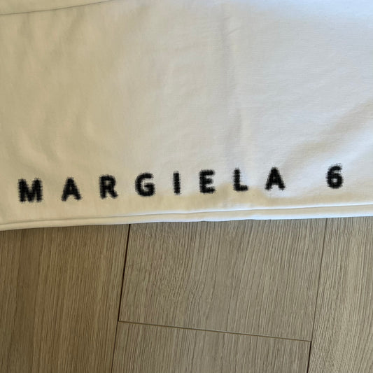 Beige fabric with 'MARGIELA 6' printed on it, on a wooden floor.