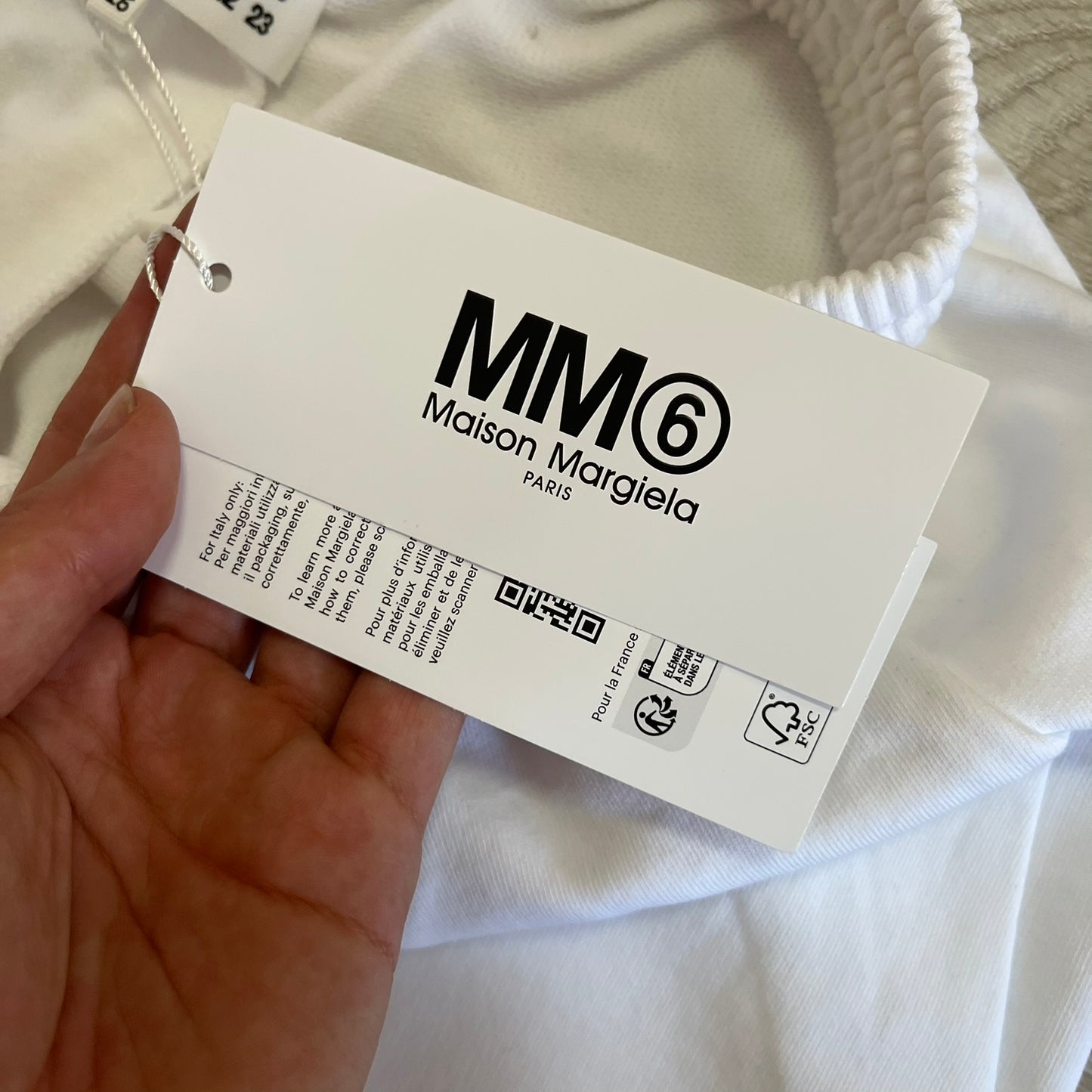 Maison Margiela label held by a hand with a white garment in the background