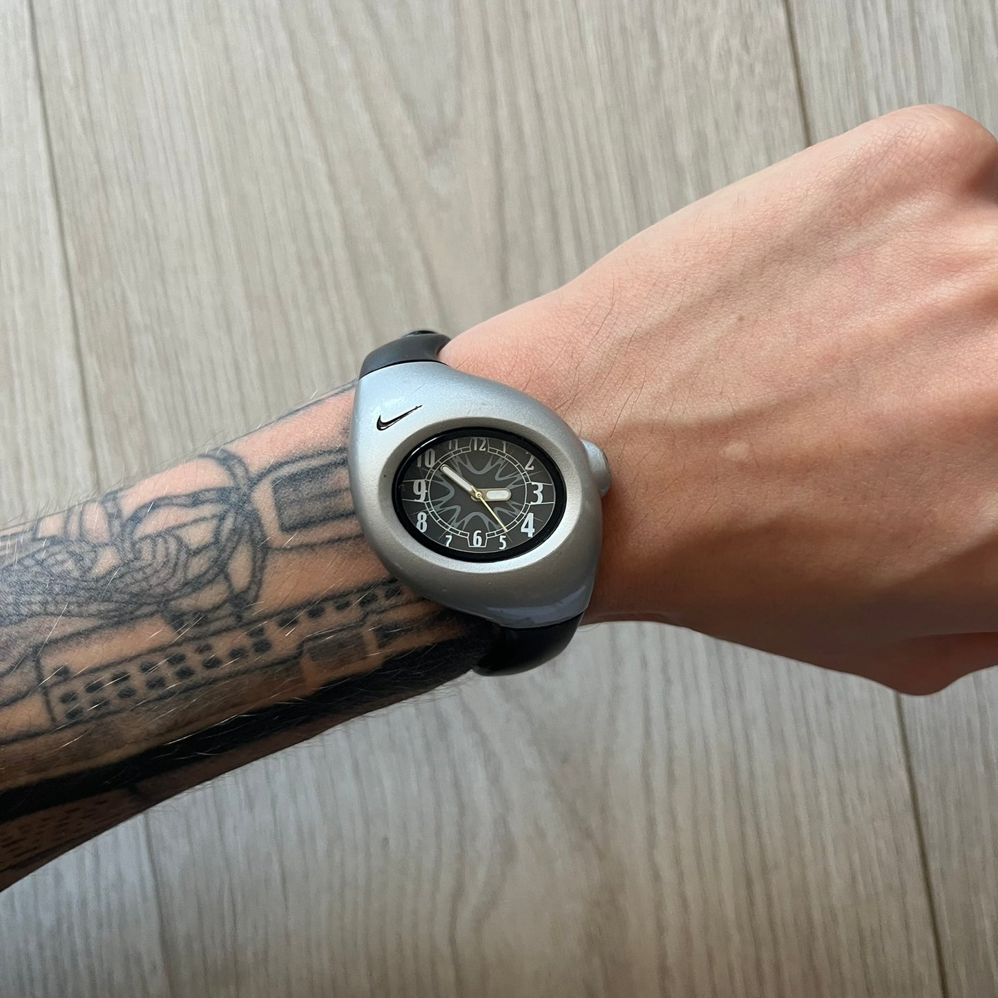 Wrist wearing a unique watch with a tattooed arm on a wooden surface