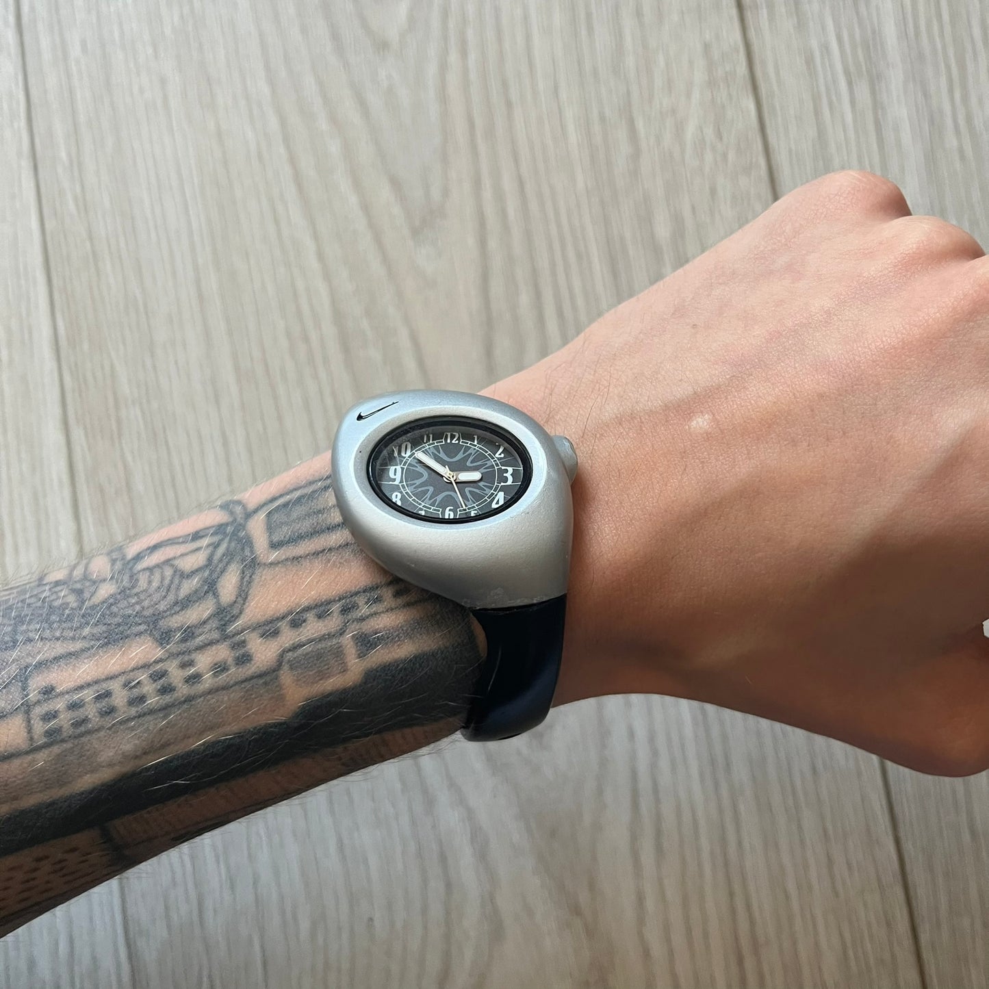 Person wearing a unique wristwatch with a black face and silver casing on a wooden surface.