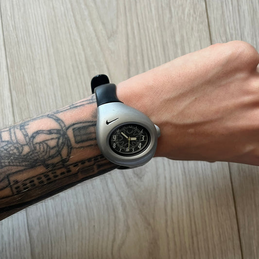 Person wearing a silver watch with a black strap on a wooden surface