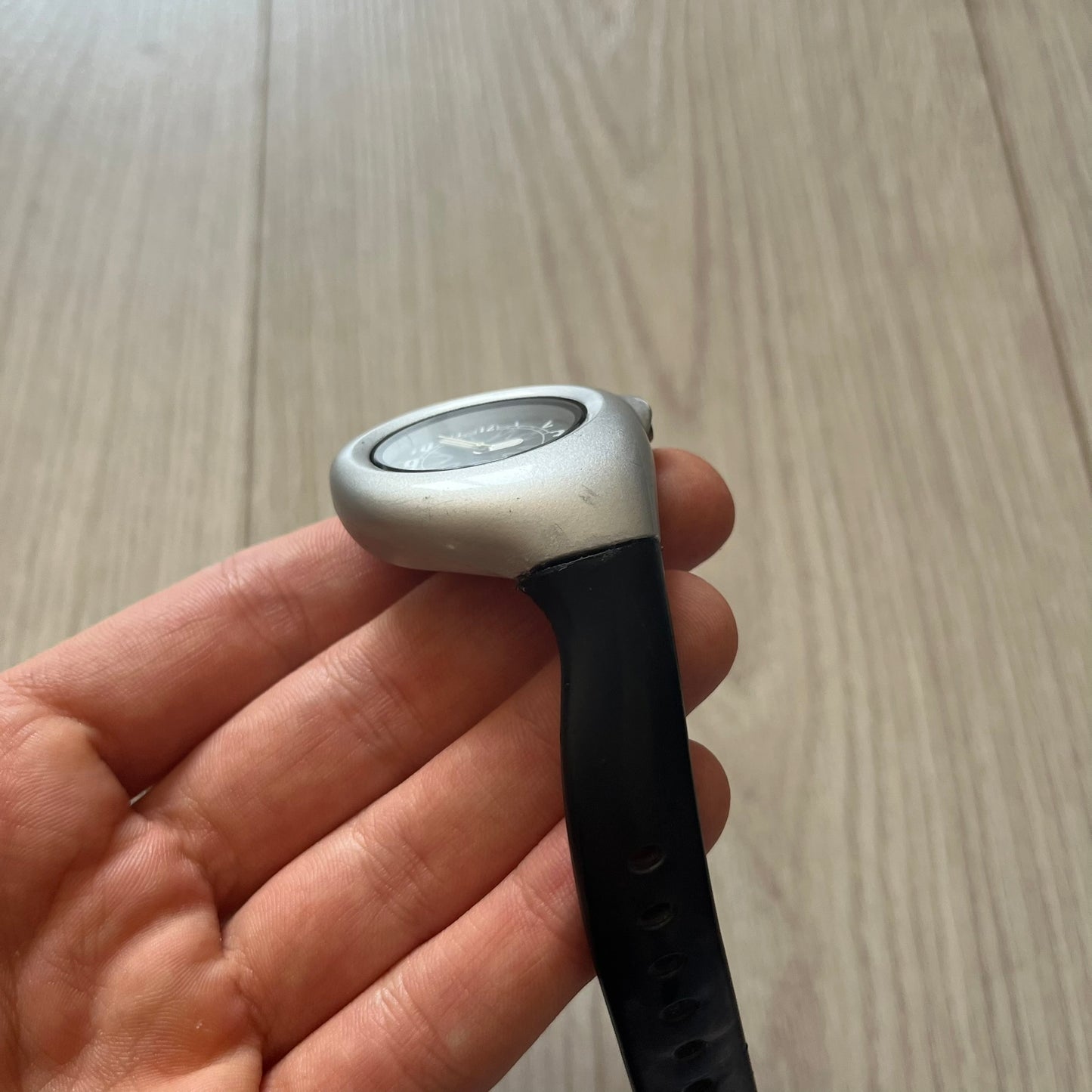 Hand holding a black and silver earbud against a wooden surface