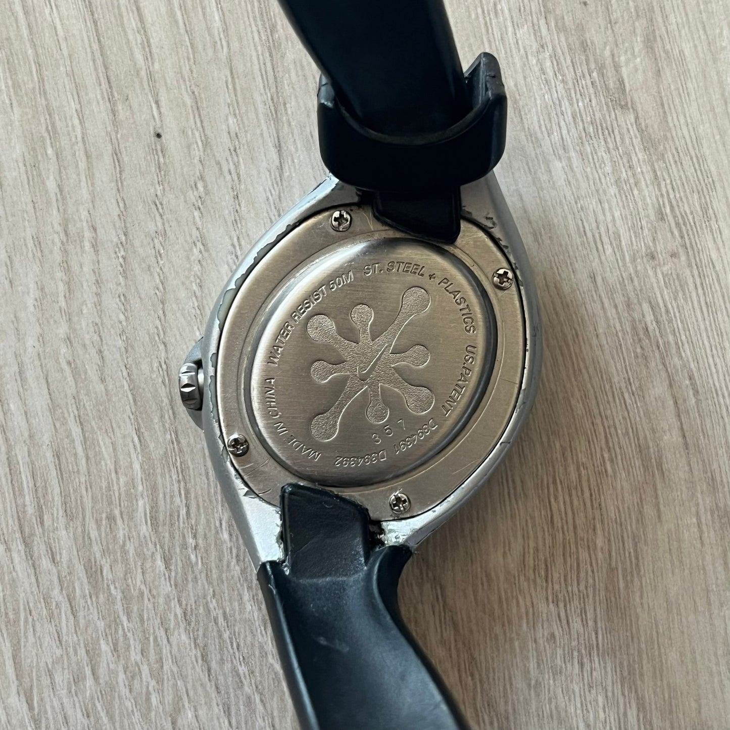 Back view of a watch with a black strap on a light wooden surface