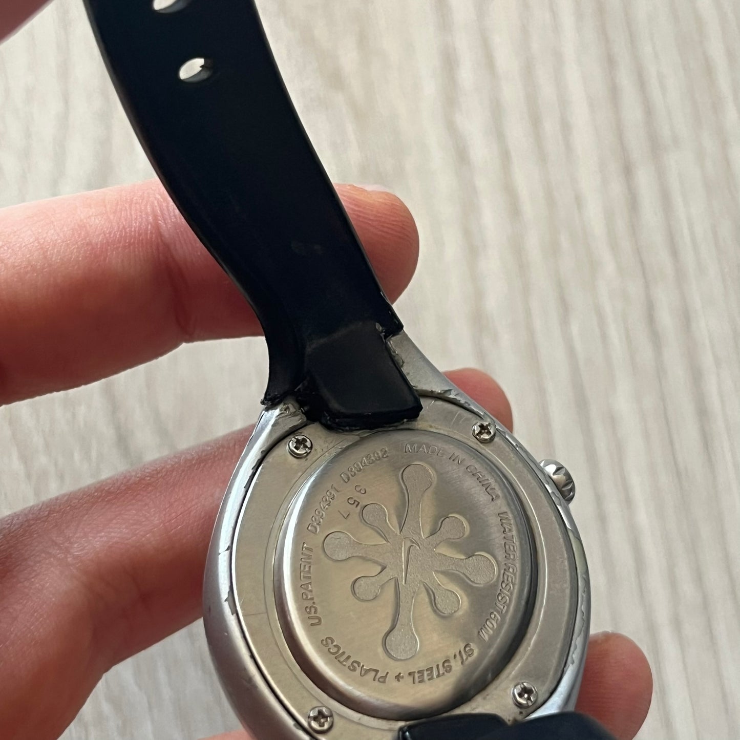 Close-up of a watch back cover with engraved design held by a hand on a light background