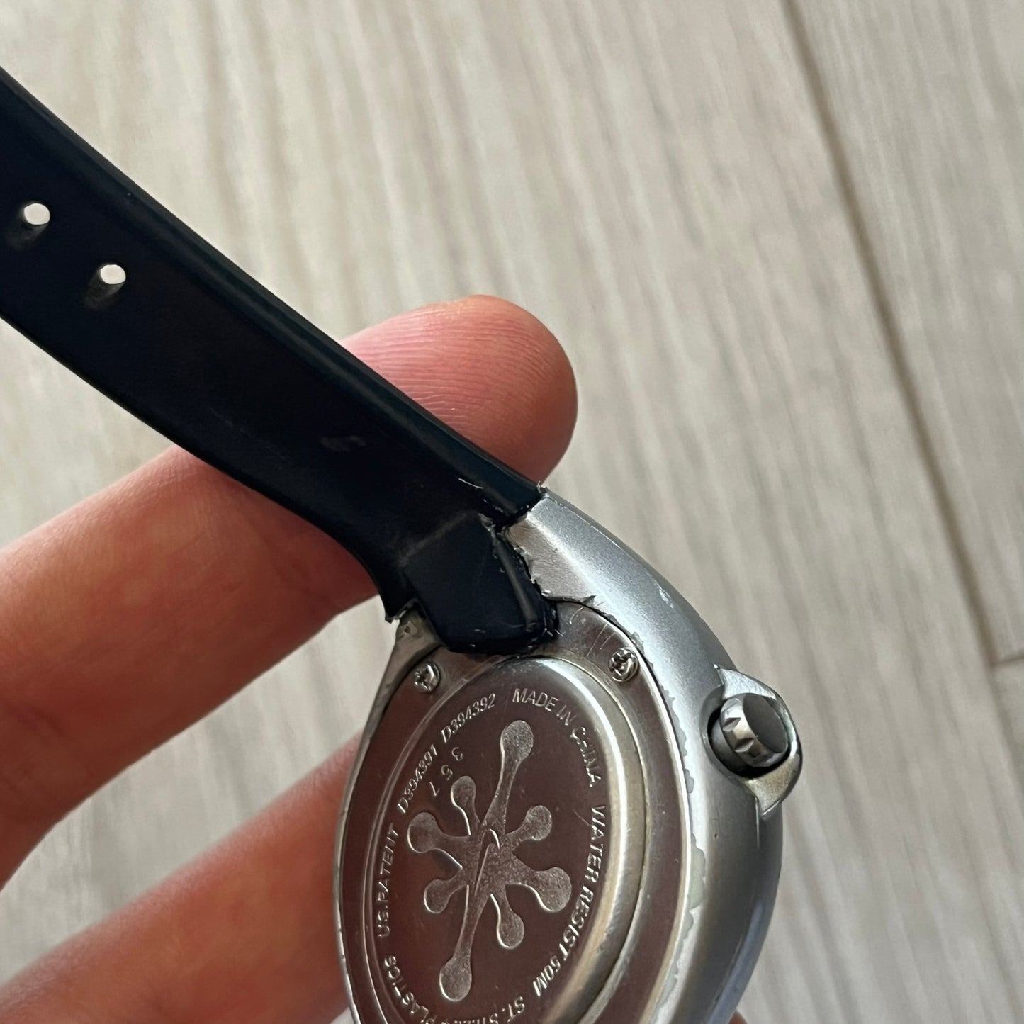 Close-up of a watch with a black strap and metal case, held by a hand on a wooden surface.