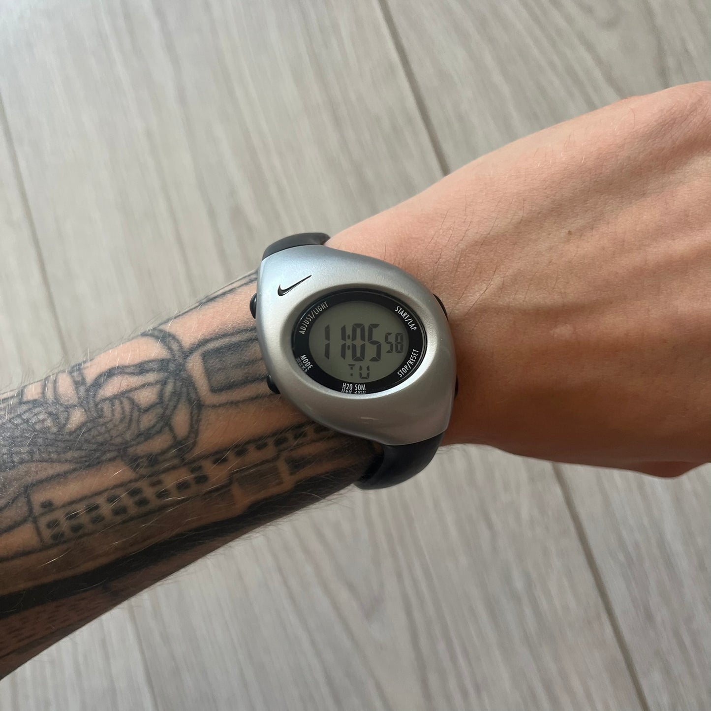 Digital watch on a wrist with tattoos, on a wooden surface
