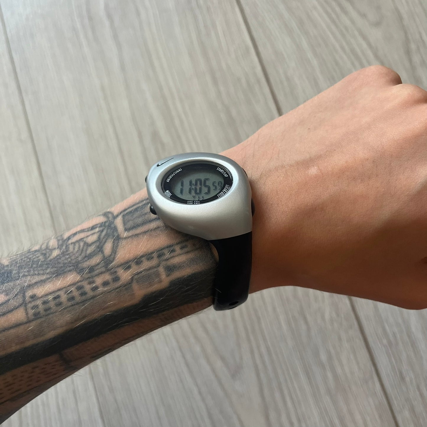 Digital watch on a wrist with a tattooed arm, on a wooden surface