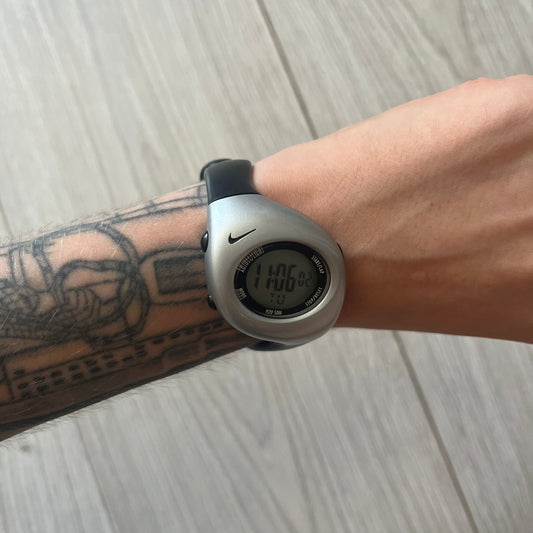 Digital watch on a wrist with tattoos on a wooden surface
