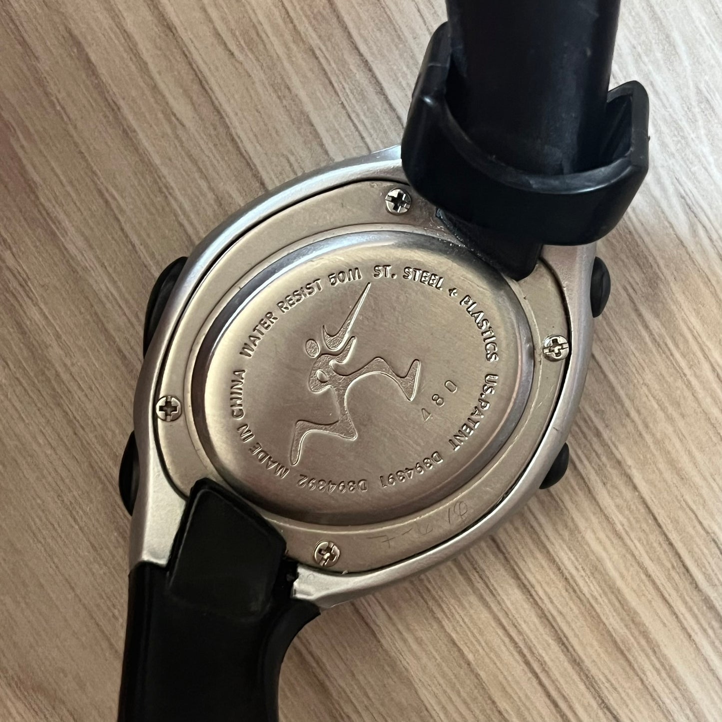 Back view of a watch with brand logo on a wooden surface