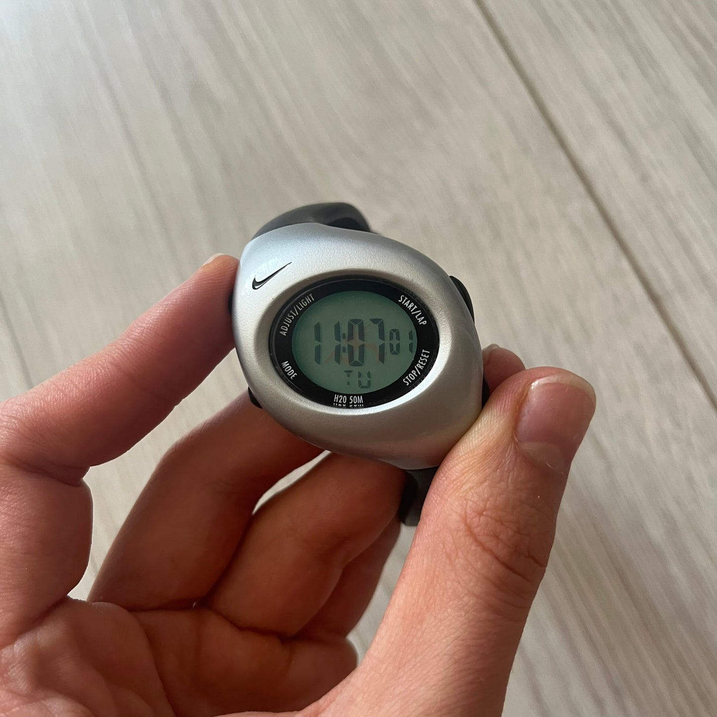 Hand holding a digital watch with a visible Nike logo on a light wooden surface