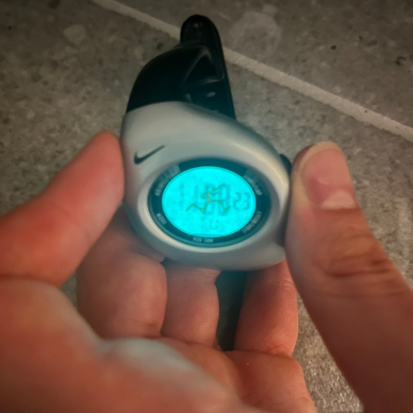 Digital watch with Nike logo held by a person on a tiled floor