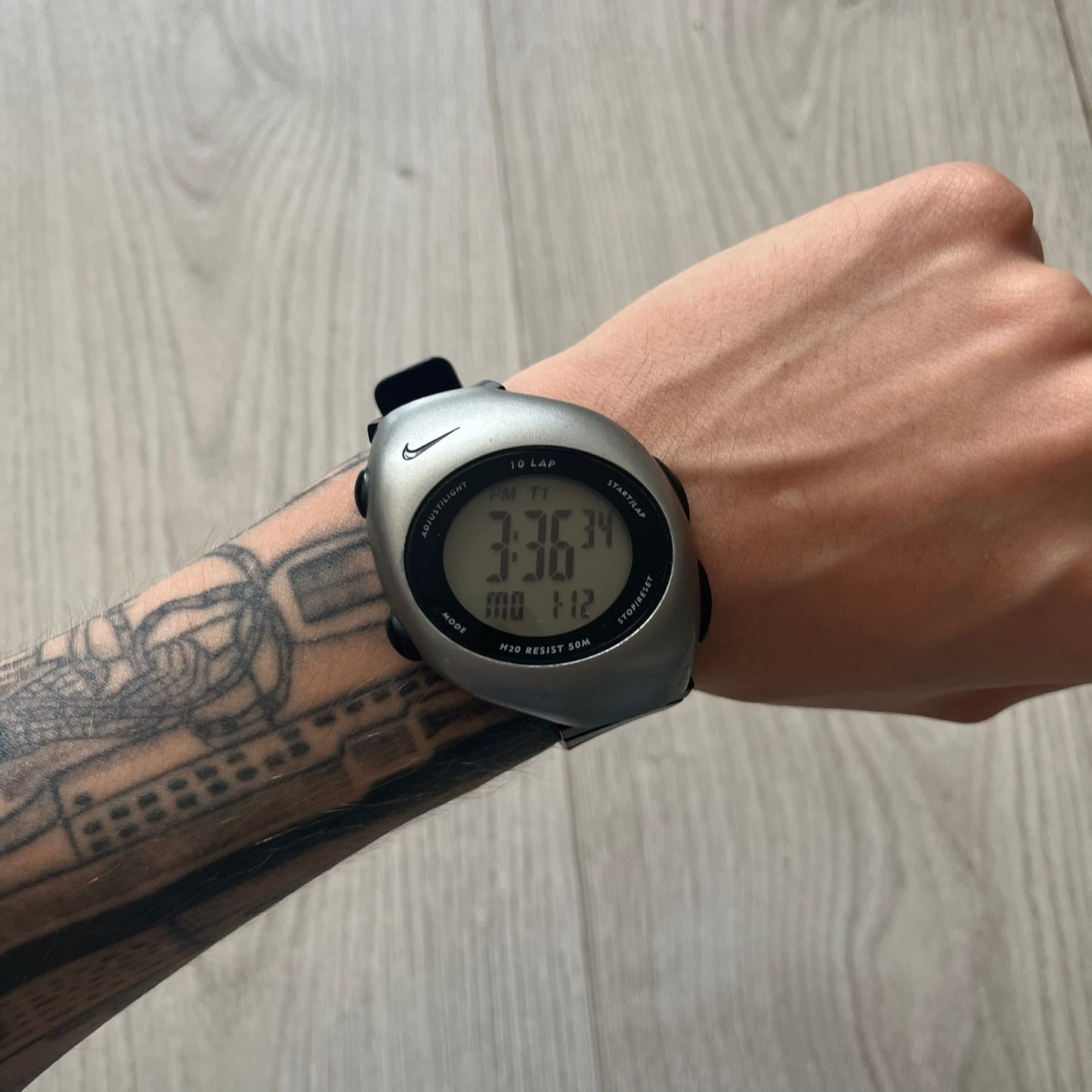 Digital watch on a wrist with tattoos against a wooden background