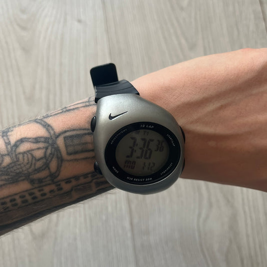 Digital watch on a wrist with a tattooed arm, on a light wooden surface