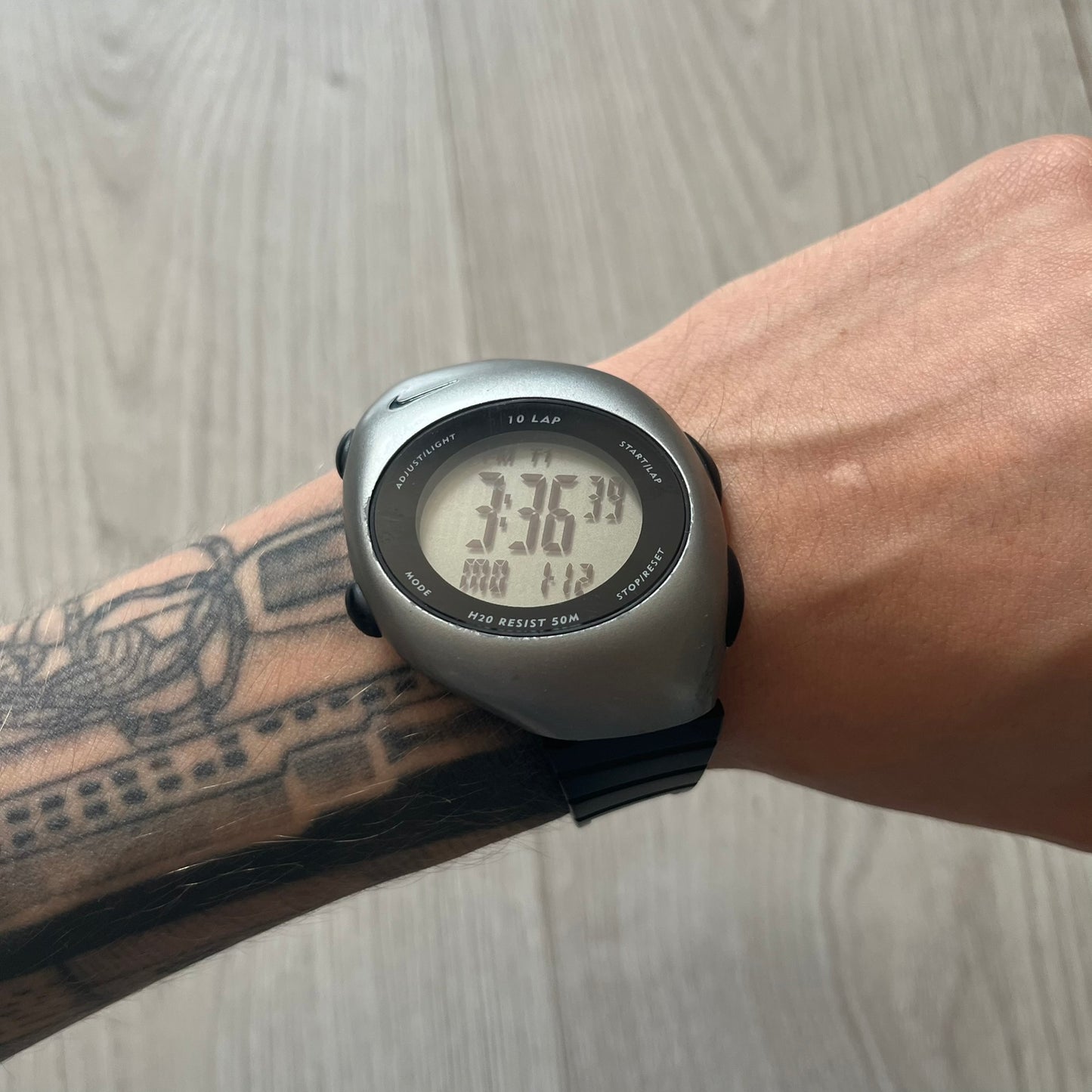 Digital watch on a wrist with a tattooed arm against a wooden surface