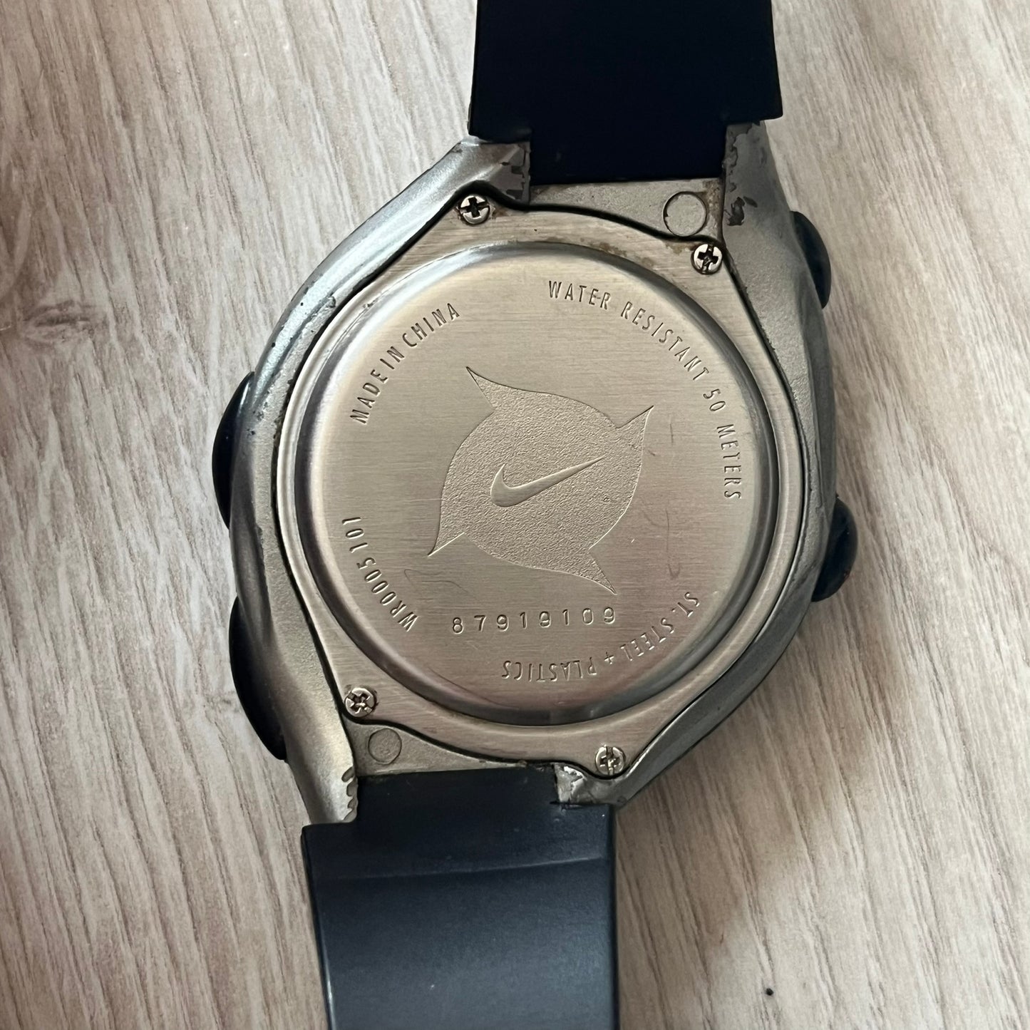 Back view of a watch with a brand logo on a wooden surface