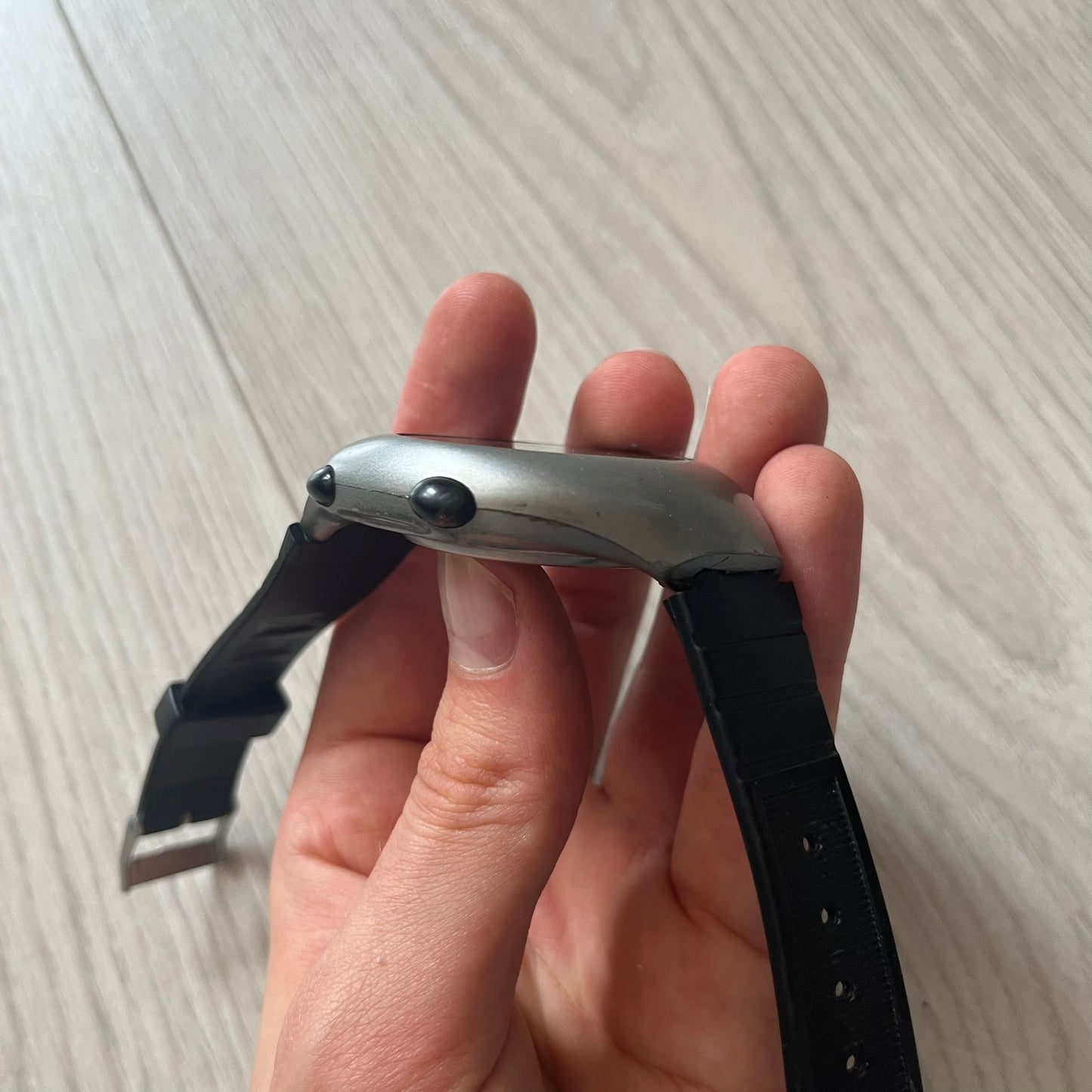 Hand holding a smartwatch with a black band on a light wooden surface