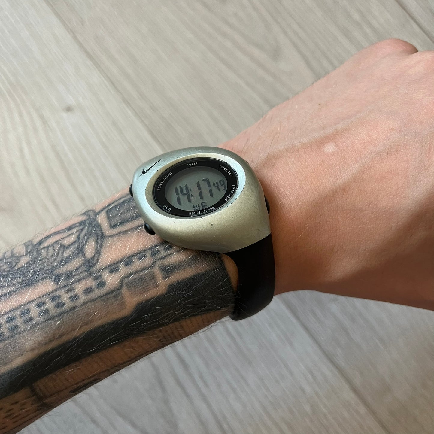 Digital watch on a wrist with tattoos on a light wooden surface