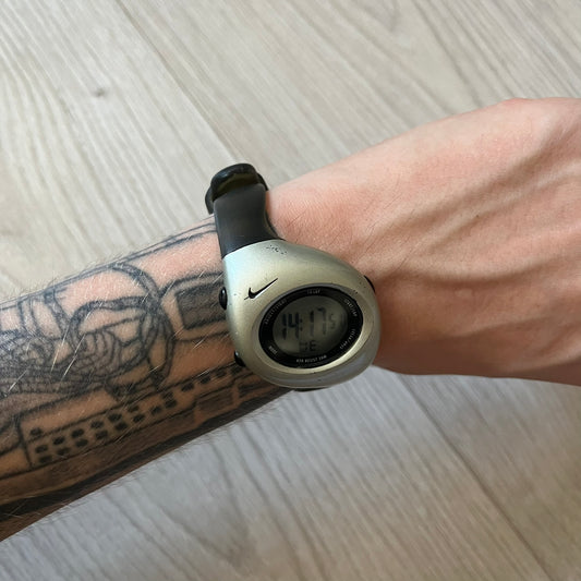 Digital watch on a wrist with a tattooed arm, on a light wooden surface