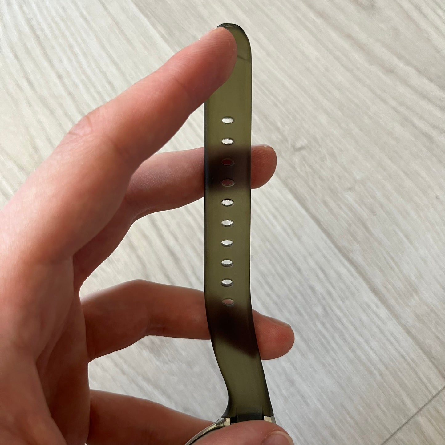 Hand holding a metallic watch strap on a light wooden surface