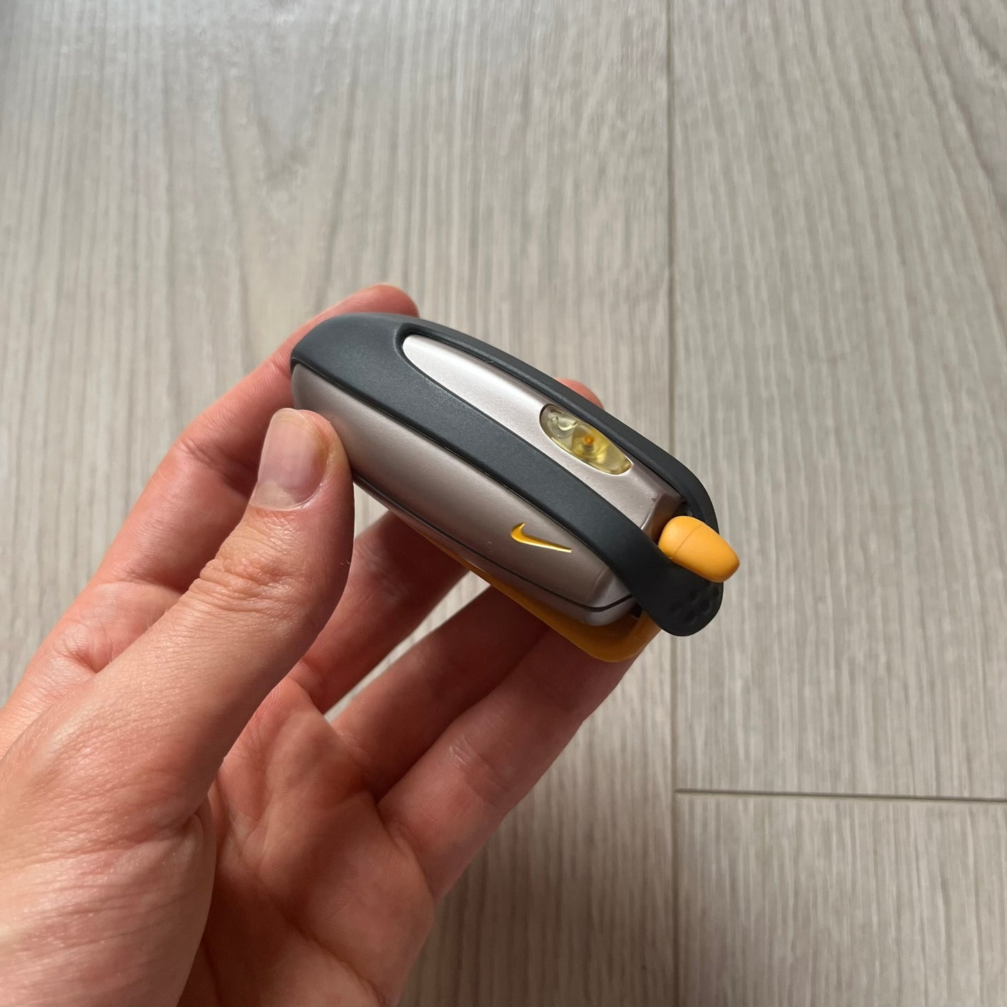 Hand holding a small flashlight with a visible brand logo on a wooden surface