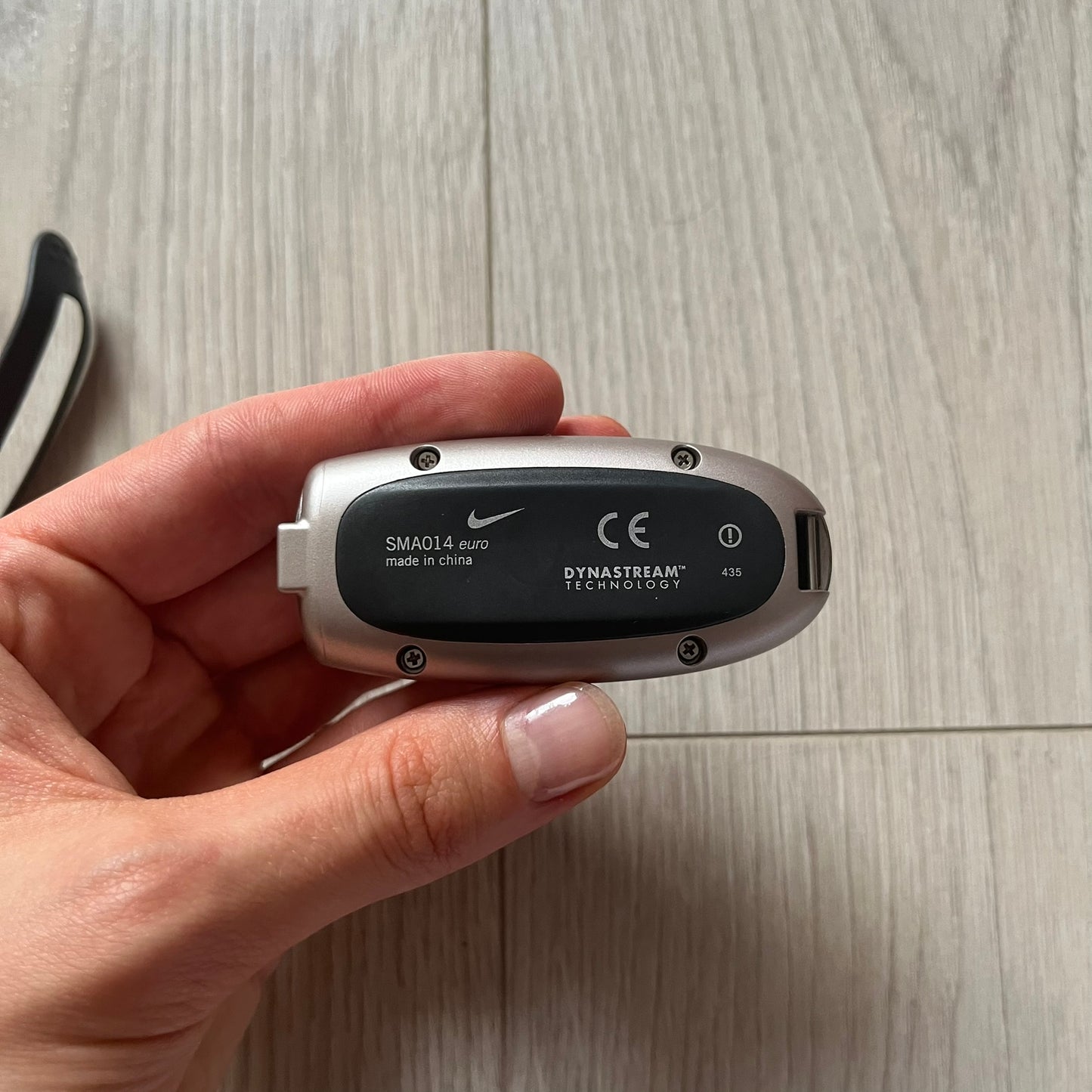 Hand holding a small electronic device with visible branding on a wooden surface