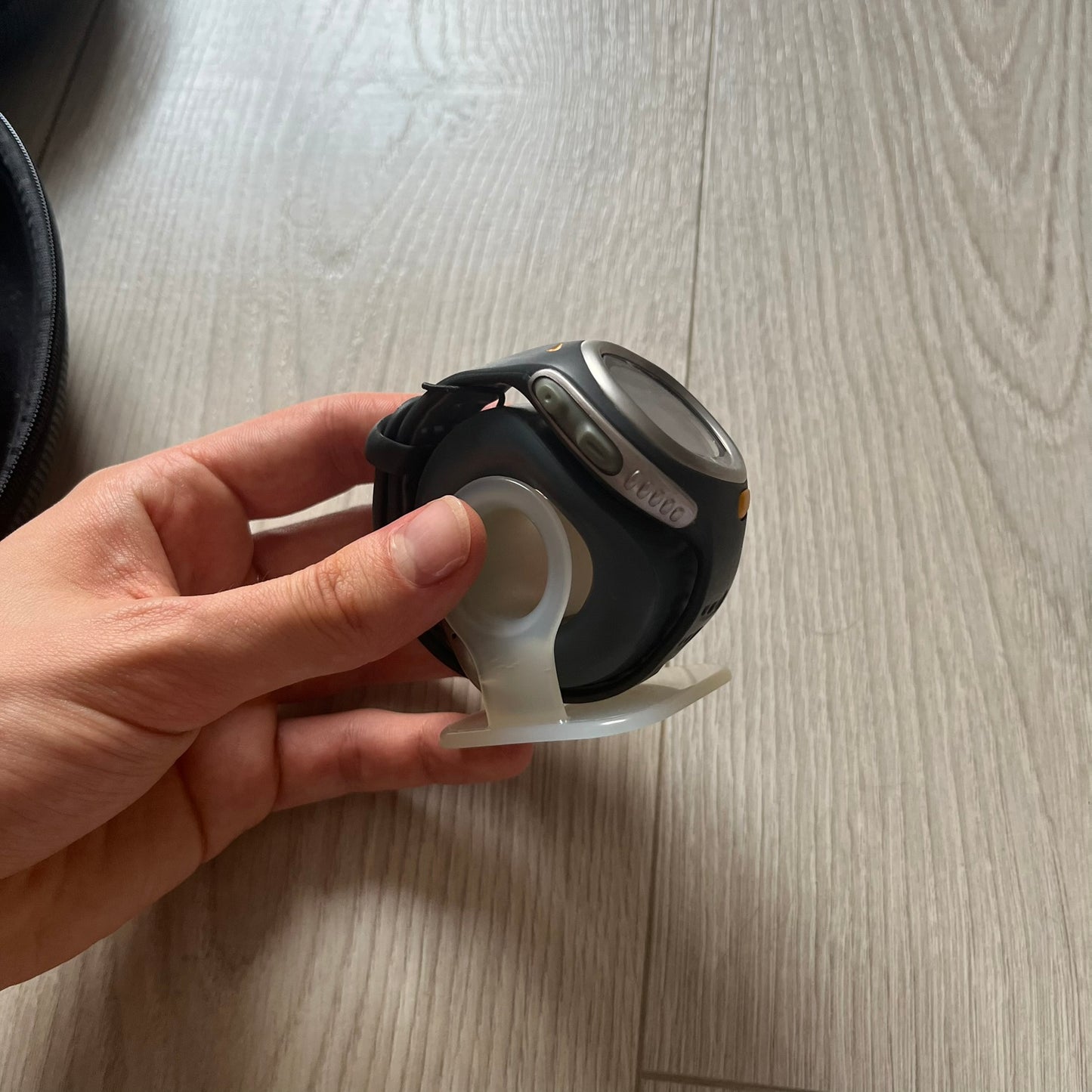 Hand holding a black watch with a white band on a wooden surface